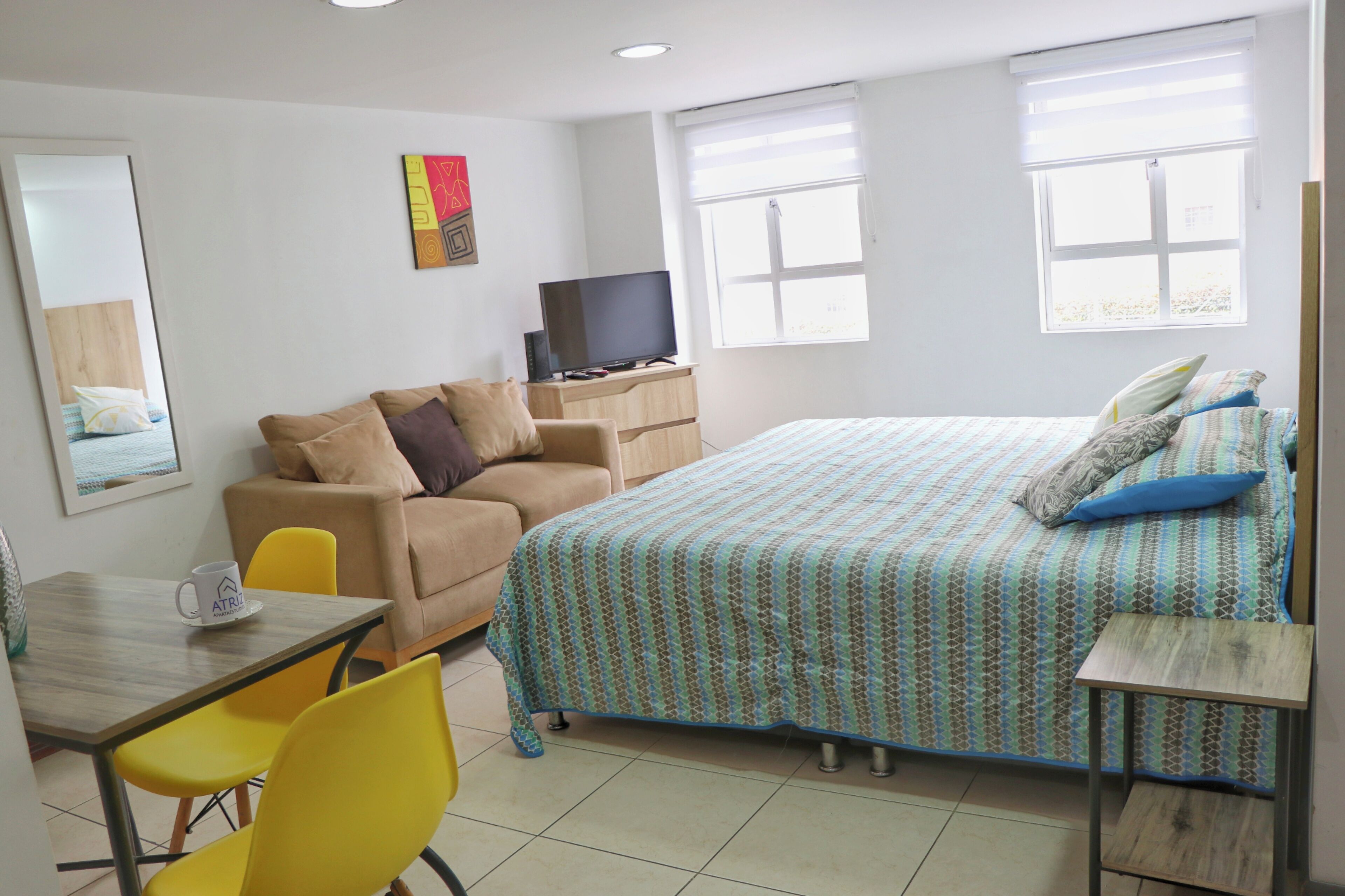 A hotel room with a bed, a sofa, a TV, a table, and chairs.