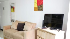 Un salon avec un canapé beige, un téléviseur posé sur un meuble et un buffet en bois.