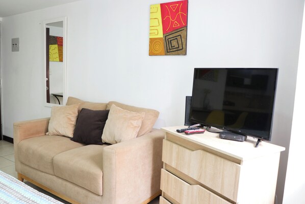 Una sala de estar con un sofá color beige, un televisor sobre un mueble bajo y un armario de madera.