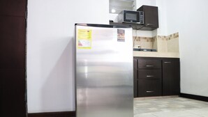 Un réfrigérateur en acier inoxydable dans une cuisine aux meubles sombres, avec un four à micro-ondes placé au-dessus.
