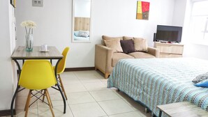 Une chambre d’hôtel avec un lit, un canapé, une télévision, une petite table et une chaise.