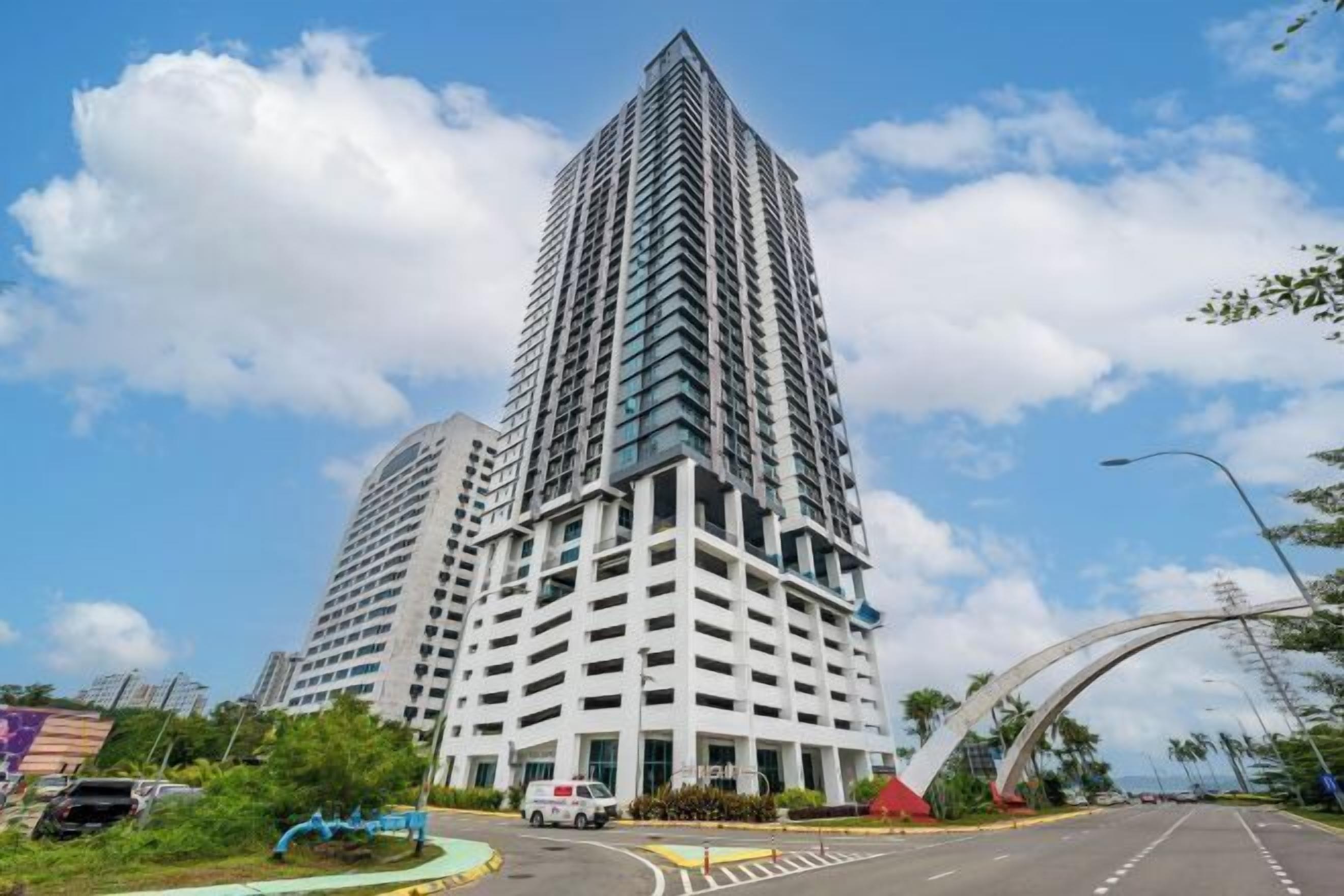 A tall, modern building with a grid-like facade, surrounded by a clear sky and a curved road structure.