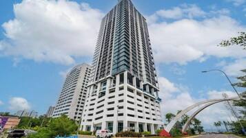 A tall, modern building with a grid-like facade, surrounded by a clear sky and a curved road structure.