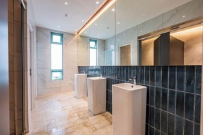 Une salle de bain moderne avec trois lavabos, de grands miroirs et un sol carrelé.