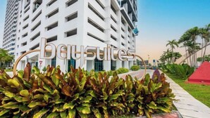 Un edificio de gran altura con un letrero que dice 'Baysuites' y un área ajardinada con plantas al frente.