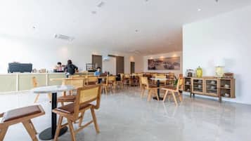 Un amplio comedor interior con múltiples mesas y sillas, una barra con una persona al final, y una pared decorada con objetos.