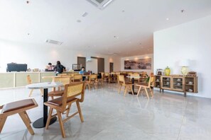 Un amplio comedor interior con múltiples mesas y sillas, una barra con una persona al final, y una pared decorada con objetos.