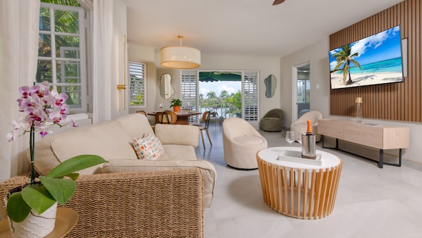 Un salon moderne avec un canapé, des fauteuils, une table basse et un téléviseur fixé au mur.