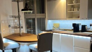 Een moderne keuken met witte kasten, een centraal eiland en een eethoek met twee stoelen.