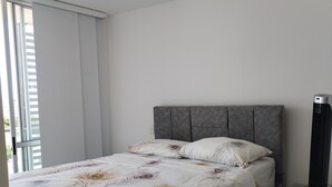 A modern bedroom with a bed, a nightstand, and a standing heater.