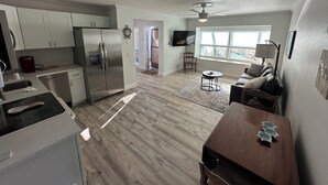 Eine moderne Küche mit Edelstahlgeräten, ein Essbereich mit Holztisch und -stühlen sowie ein Wohnzimmer mit Sofa und Fernseher.