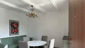 A dining area with a round table, grey upholstered chairs, a green sofa, a chandelier, and a framed abstract artwork on the wall. - Sormano 1 - THE V Collection Apartment by OGS (Sormano)
