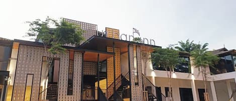 Um edifício moderno com escadaria que leva a uma entrada coberta, cercado por vegetação e palmeiras.