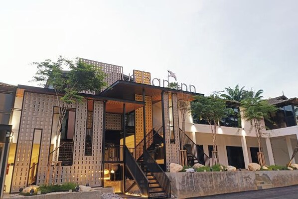 A modern building with a staircase leading to a covered entrance, surrounded by greenery and palm trees.