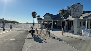 Un edificio frente a la playa con un letrero que indica Palm Pavilion, un restaurante y bar junto a la playa, y un área de estacionamiento designada.