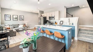 Une cuisine moderne dotée d’un îlot central, un coin repas avec une table et des chaises, et un salon avec un canapé et une table basse.