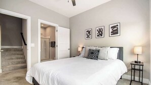 Une chambre à coucher avec un grand lit, une table de chevet, une lampe et une porte donnant sur une salle de bain.