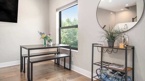 Une pièce avec un plancher en bois, un banc en métal noir, un miroir rond et une fenêtre donnant sur des arbres.