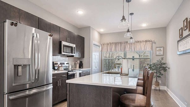 A modern kitchen with stainless steel appliances, a central island, and a dining area with bar stools. - Trendy Townhouse in Midtown Omaha|Rooftop Retreat (Omaha)