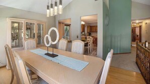 Ein Essbereich mit einem Holztisch, Stühlen und einer Chandelier. Eine Küche ist im Hintergrund zu sehen.