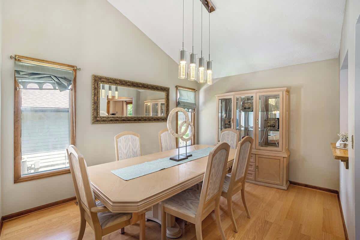 Un comedor con una mesa de madera, seis sillas, una araña, un espejo grande y un aparador con puertas de cristal.