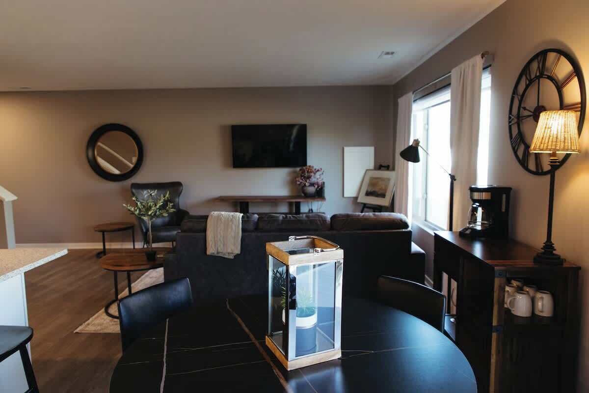 Un salon moderne avec une table basse ronde, une table d’appoint avec un plateau en verre, un canapé et un téléviseur fixé au mur.