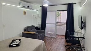 Et moderne hotelværelse med seng, skrivebord, stol, fjernsyn og en balkon med gardiner.