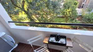 En balkon med udsigt over en have, et lille bord med kaffemaskine og to hvide stole.