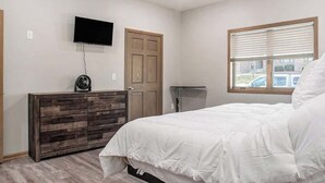 A bedroom with a bed, a dresser, a television on the wall, and a window with blinds. - Accessible Escape- Completely Handicap accessible! (Council Bluffs)