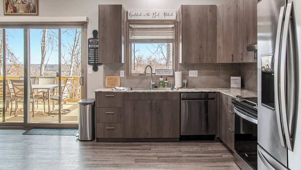 A modern kitchen with dark wood cabinets, a stainless steel refrigerator, and a window with a view of the outdoors. - Accessible Escape- Completely Handicap accessible! (Council Bluffs)