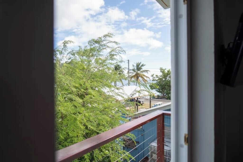 A view from a balcony with a metal railing, overlooking a street with palm trees and a clear sky.