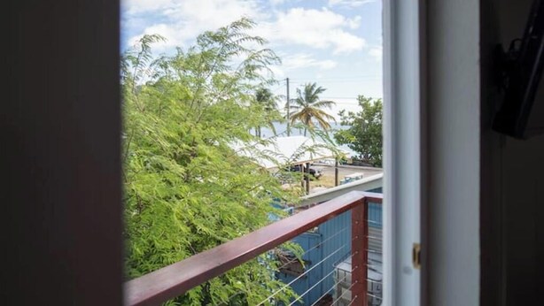 A view from a balcony with a metal railing, overlooking a street with palm trees and a clear sky. - Irie Heights Oceanview (Gros Islet)
