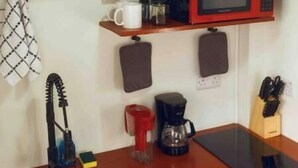 A compact kitchen with a sink, a microwave, a coffee maker, and a shelf with glasses and a mug. - Irie Heights Oceanview (Gros Islet)