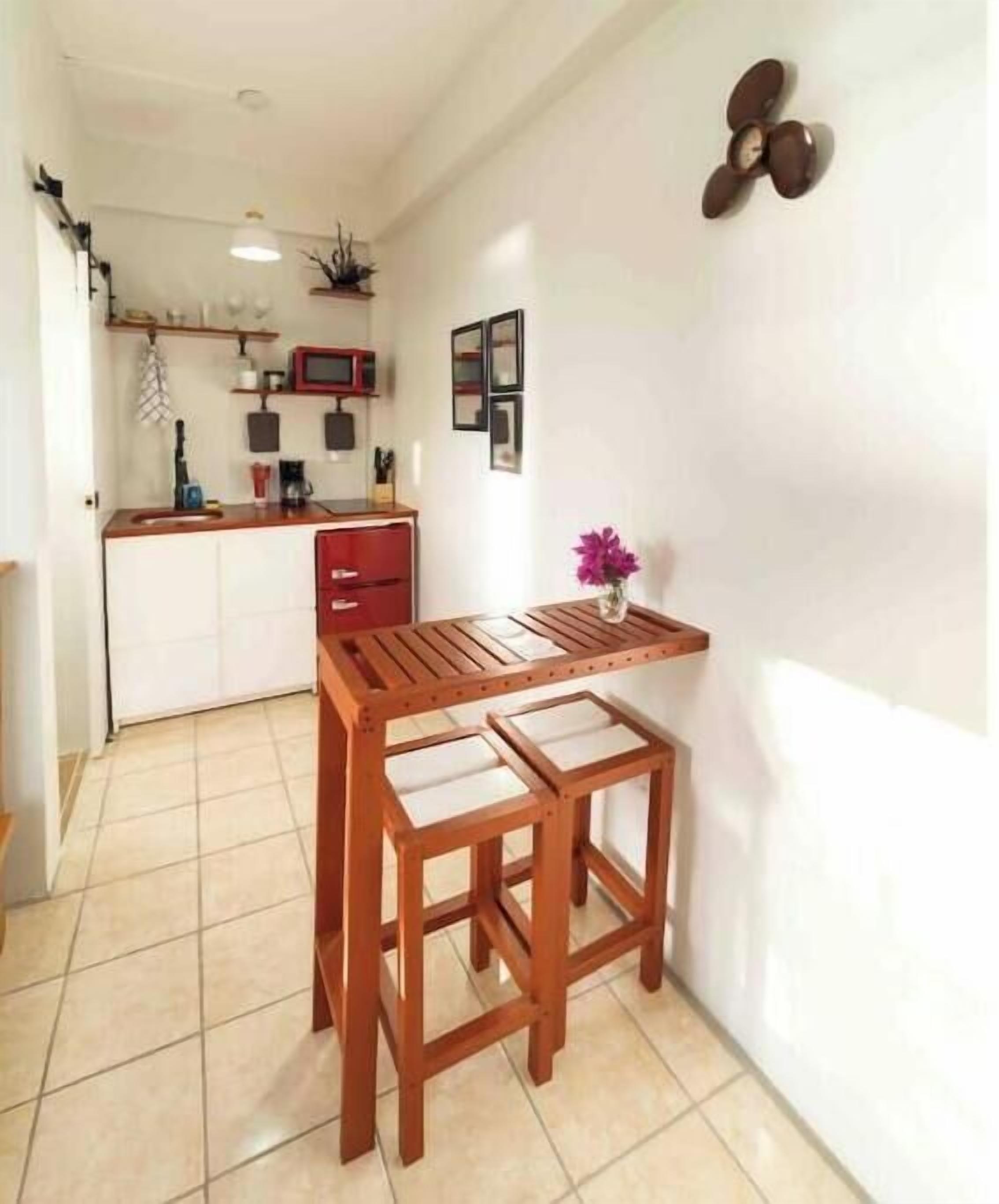 A compact kitchen with a wooden table and two stools, a small island with a sink, and a wall-mounted light fixture.