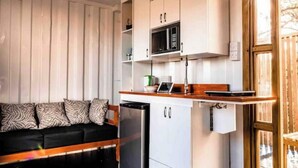 A compact kitchen with white cabinets, a microwave, and a small refrigerator. - Unique Container Home with Open Air Bathroom (Gros Islet)