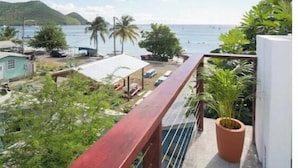 Ein Balkon mit Blick auf das Meer, ein kleiner Gartenbereich und ein Gebäude mit weißer Fassade.