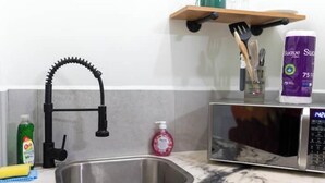 A kitchen with a stainless steel sink, a black faucet, a microwave, and a shelf with kitchen utensils and a bag of sugar. - Irie Heights Reggae Studio (Gros Islet)