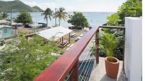 A balcony with a view of the sea, a small garden area, and a building with a white facade. - Irie Heights Reggae Studio (Gros Islet)