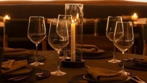 Un restaurant à la lumière tamisée, avec des tables éclairées par des bougies, de beaux verres et une vue sur la ville grâce à de grandes fenêtres.