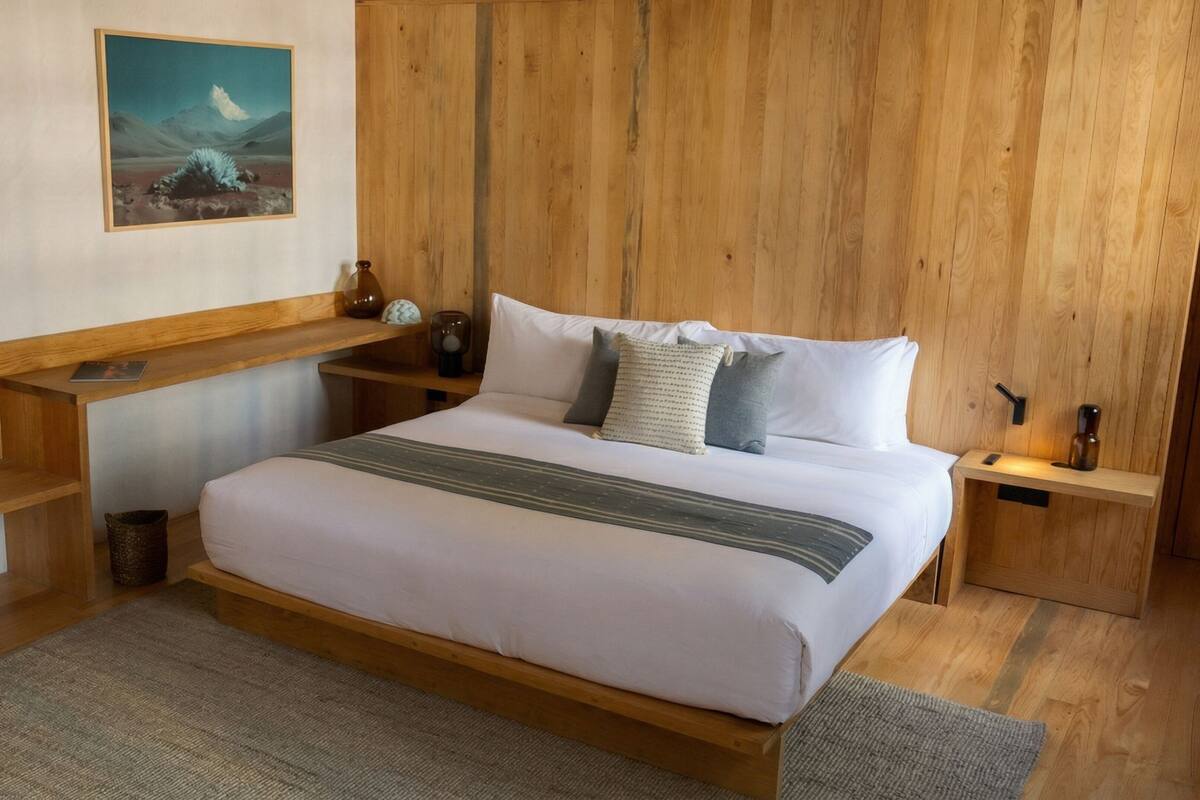 Een kamer met houten lambrisering, een bed, nachtkastje, plank en een schilderij aan de muur.