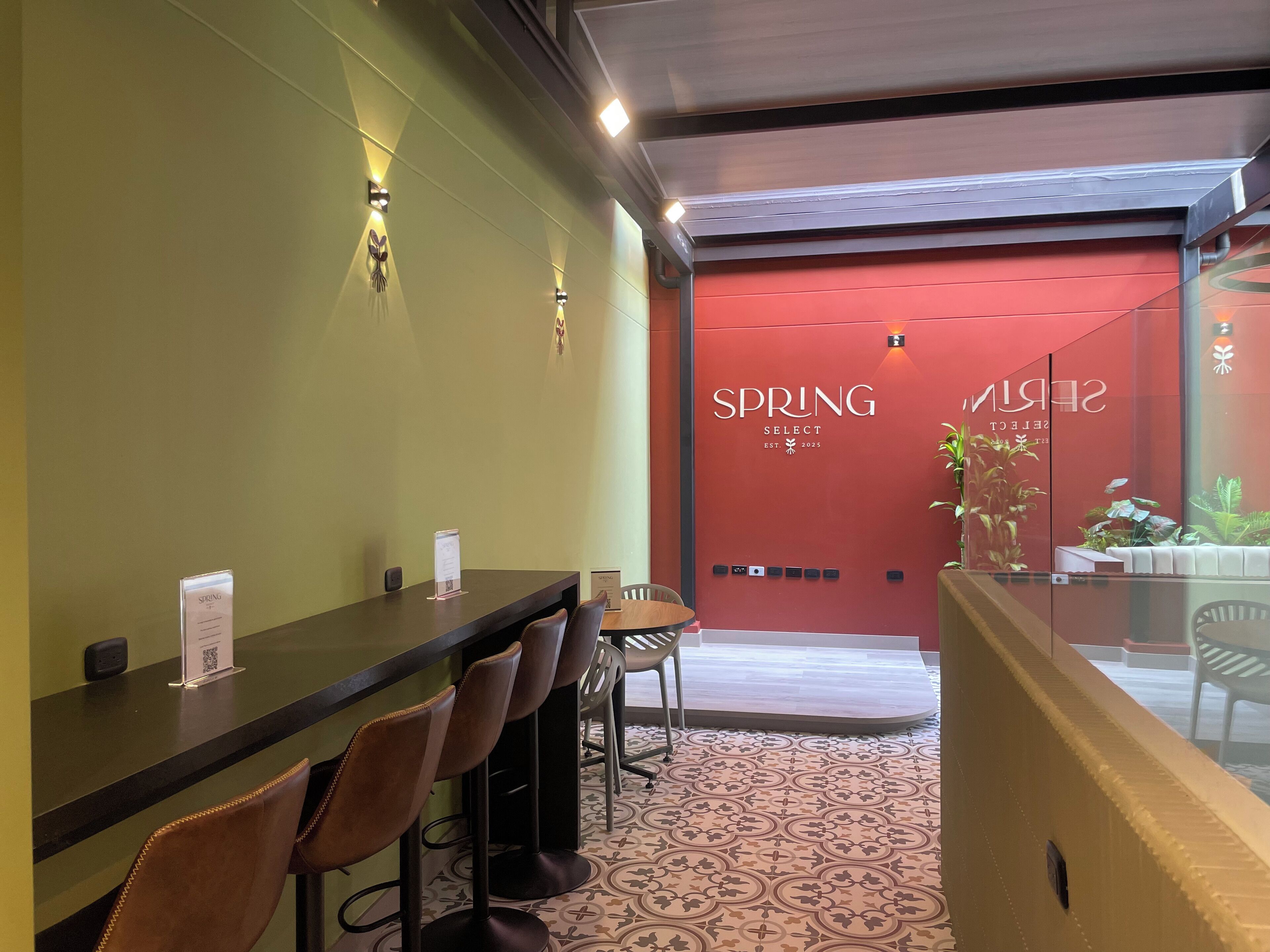 A reception area with a counter, chairs, and a red wall with the text "SPRING SELECT EST. 2025".