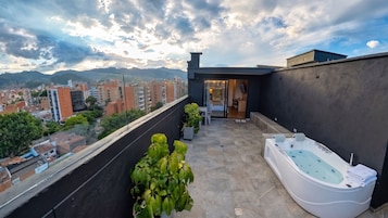 A rooftop terrace with a hot tub, potted plants, and a view of the cityscape.