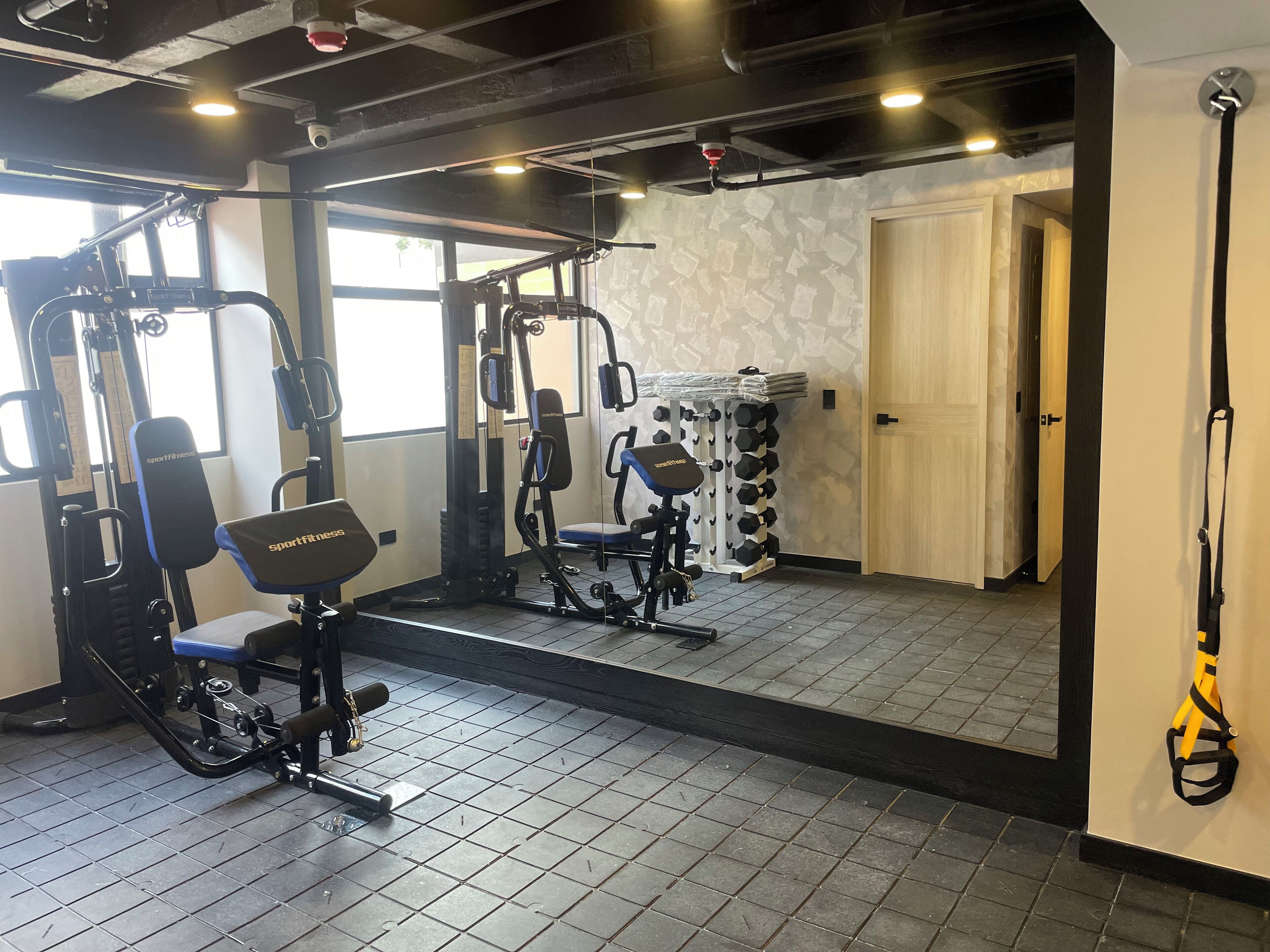 A gym with exercise equipment, a large mirror, and a door leading to another room.