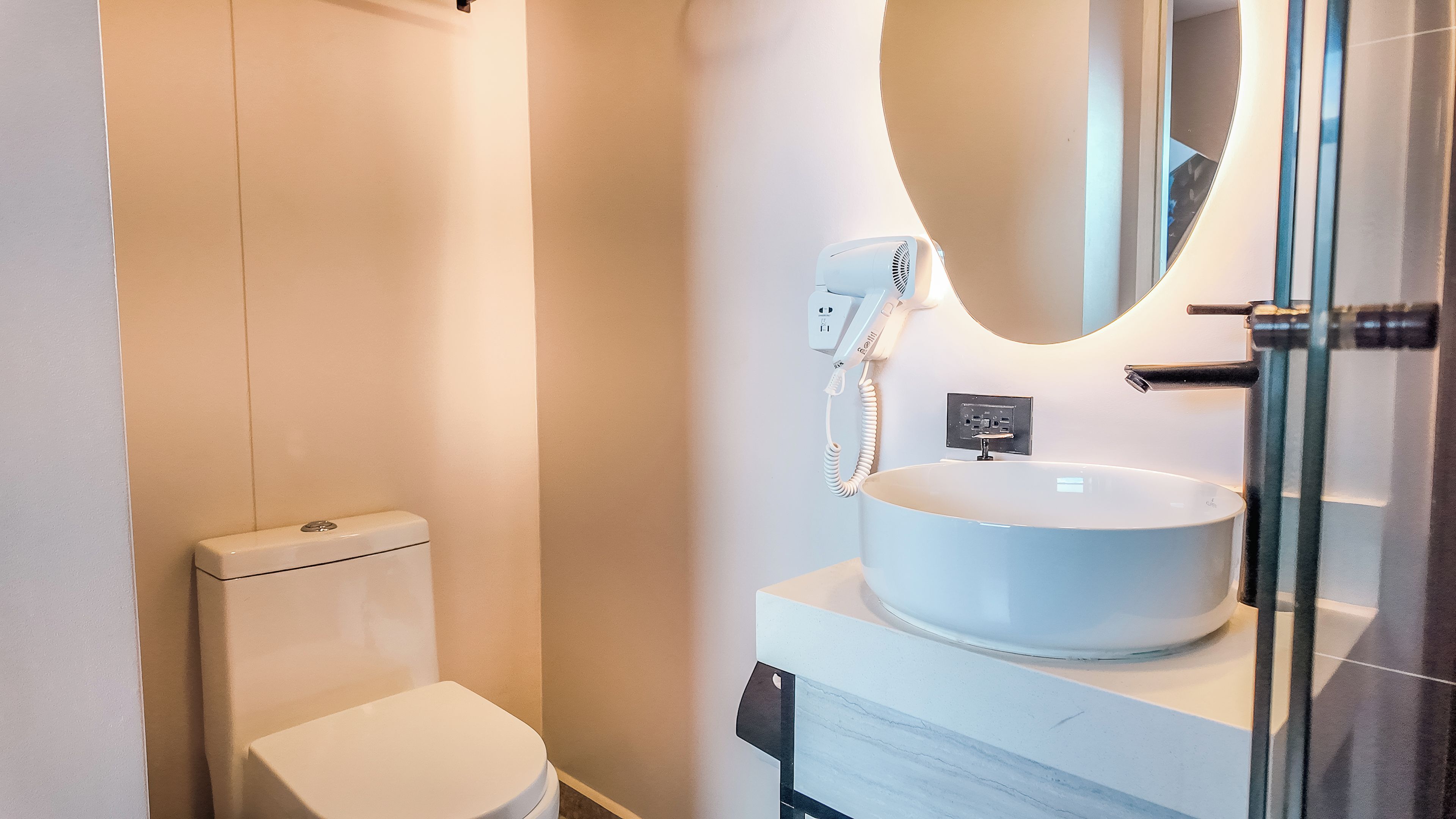 Un baño moderno con inodoro, lavamanos con un espejo grande y zona de ducha.