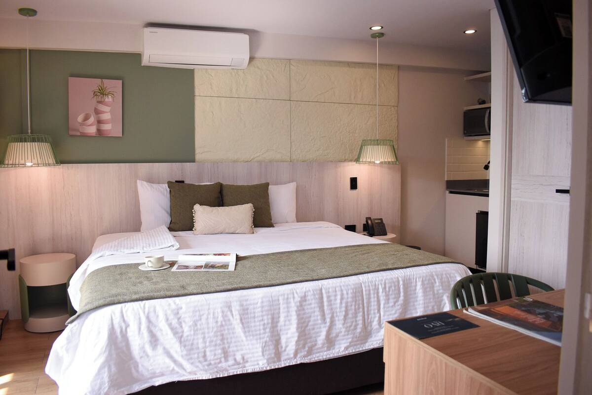A hotel room with a bed, bedside table, lamp, and a small kitchenette.