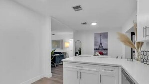 Une cuisine moderne avec des meubles blancs, un îlot central et une vue sur la Tour Eiffel par une fenêtre.