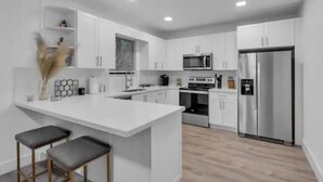 Une cuisine moderne avec des meubles blancs, un îlot central doté de tabourets, des appareils en acier inoxydable et une plante décorative.