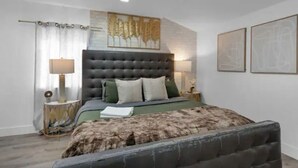 Une chambre à coucher moderne avec une tête de lit capitonnée, un grand lit, une table de chevet et un élément décoratif mural.