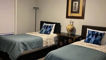 Una habitación con dos camas, cada una con cubrecama y almohadas a juego. Hay un ventilador de techo, una lámpara de pie y un cuadro en la pared.