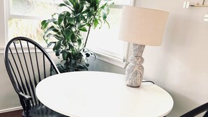 A round white table with a woven lamp, surrounded by black chairs, in a room with wooden flooring and a potted plant.